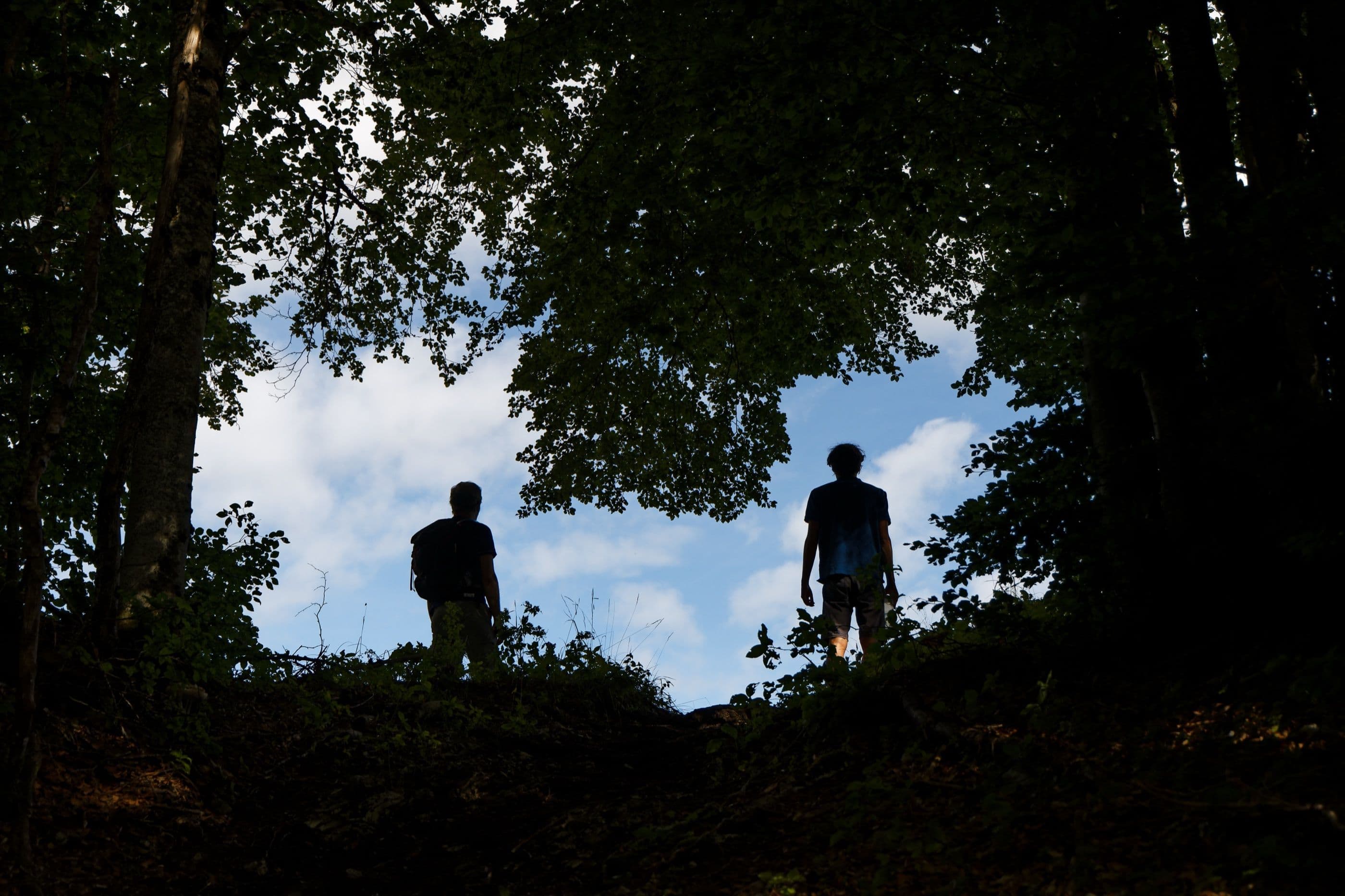 Deux silhouettes en contre-jour au sommet d'un sentier, trouée de ciel bleu